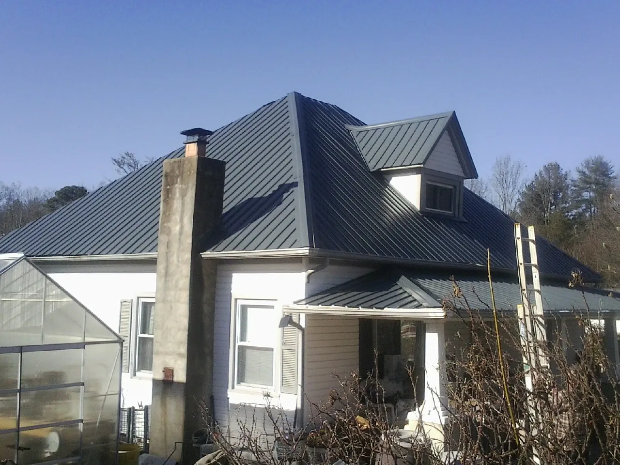 Dark blue standing seam metal roof on a white farmhouse with dormer — Slate & Tile Roof Repair by Roofing Brothers in Lowry