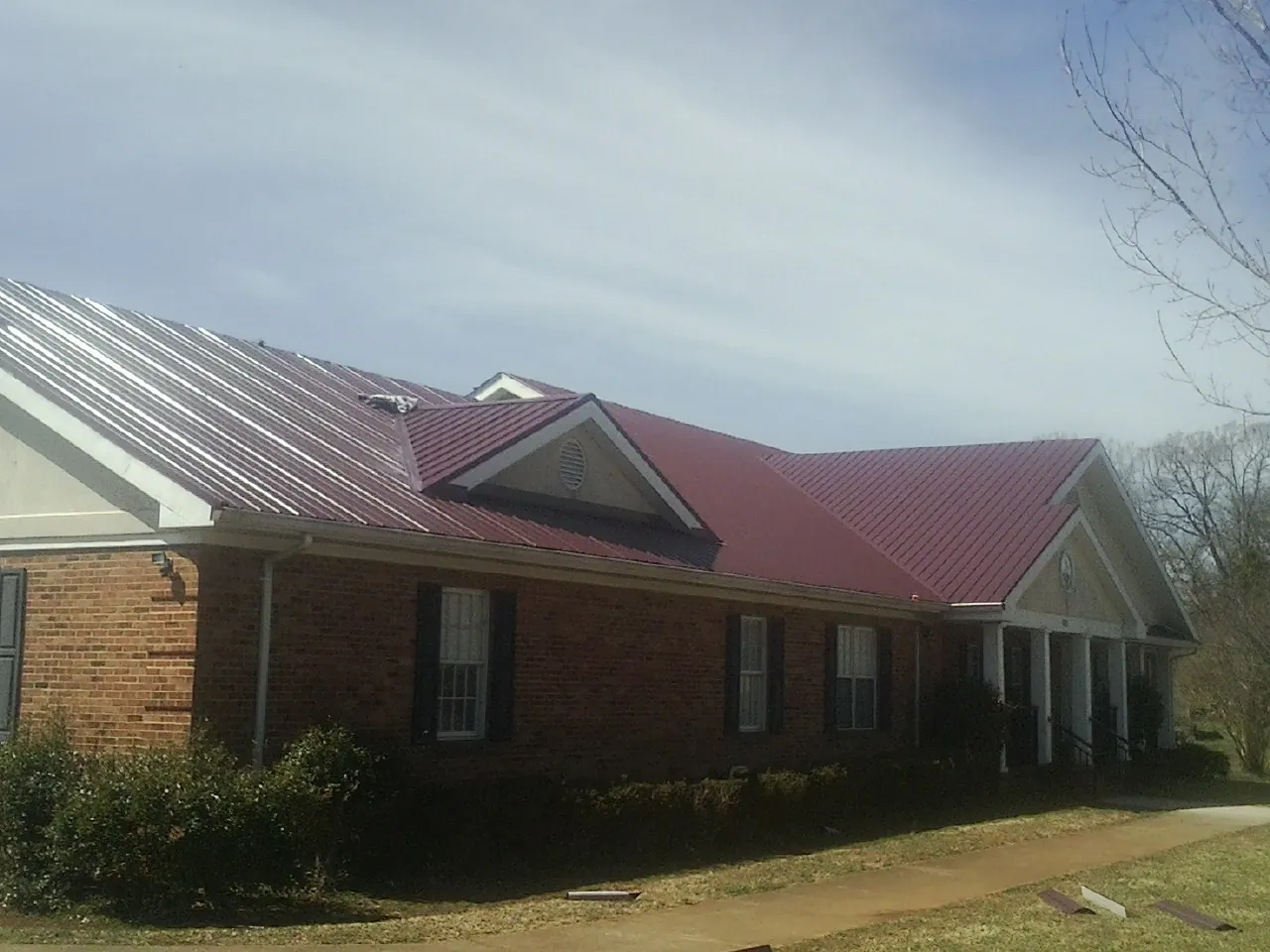 Red metal roof with gabled entries on a long brick building, from a Hail Damage Roof Repair job in Lowry