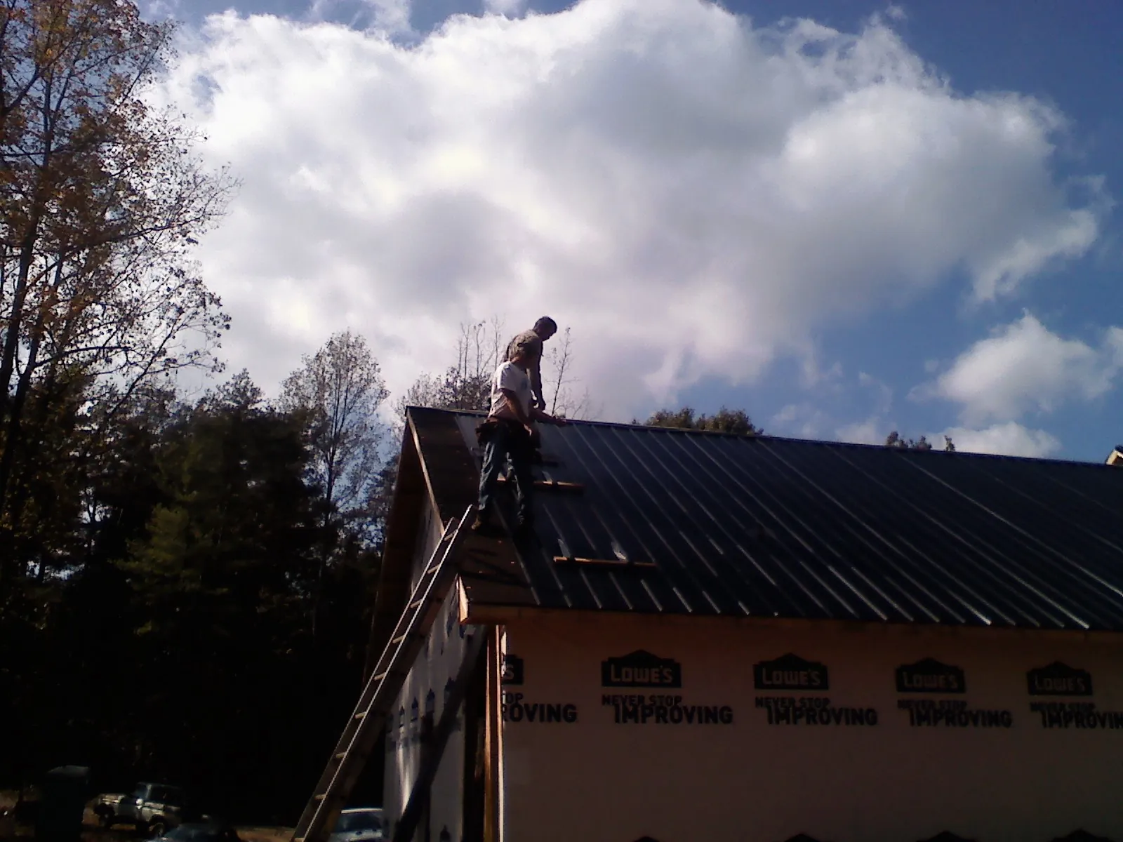 Roofer fastening dark metal panels high against a cloudy sky, from a Roof Inspection job in Lowry